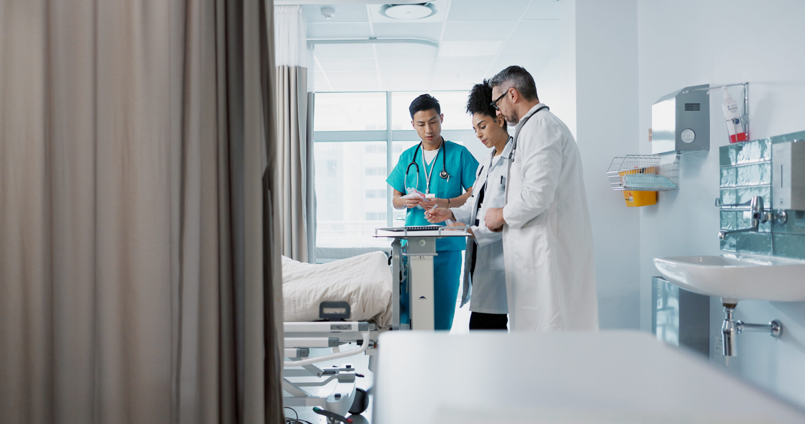 Doctors and nurses discuss patient treatment and condition at the foot of a hospital bed.