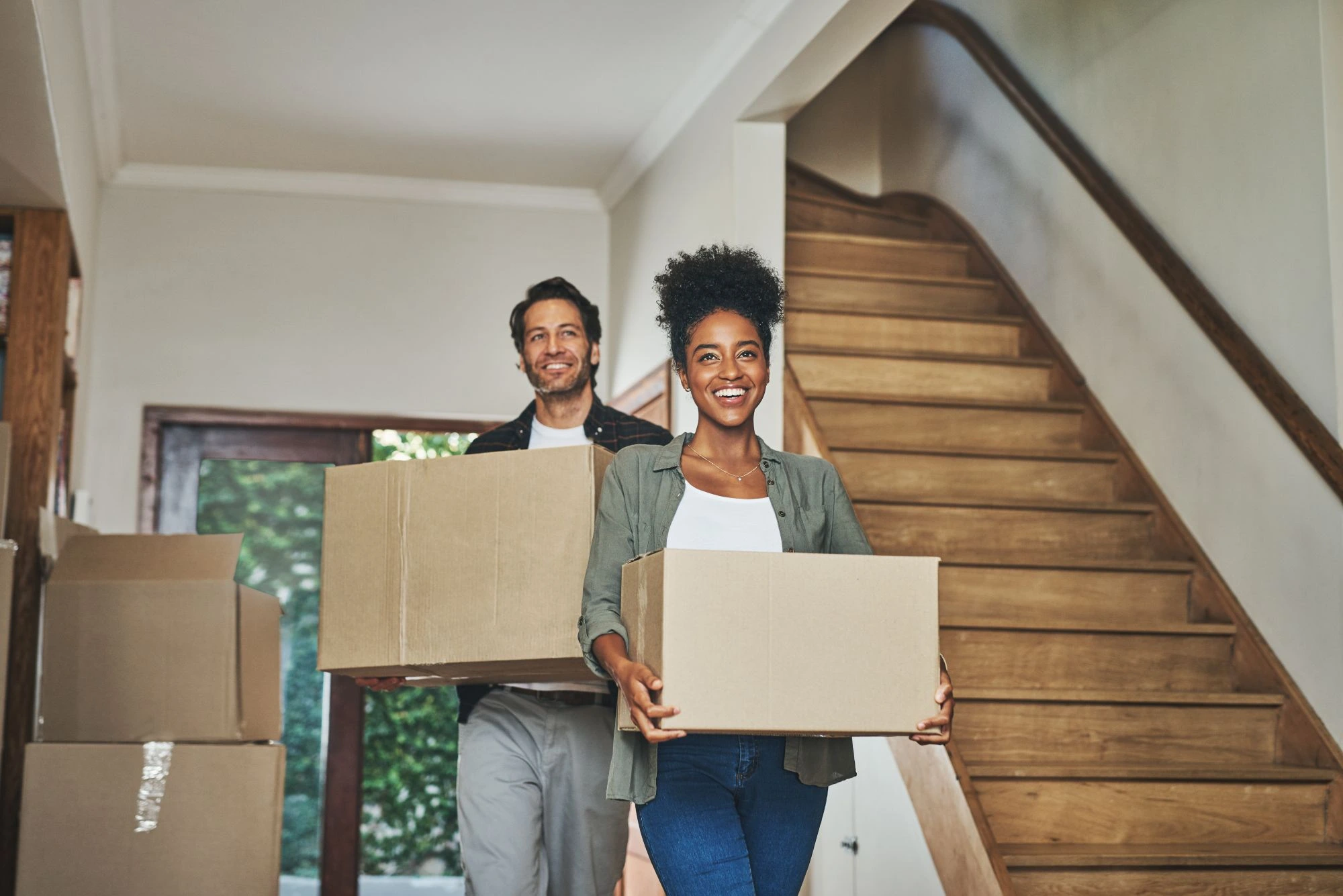 A young couple carrying cardboard boxes of belongings into their new house.